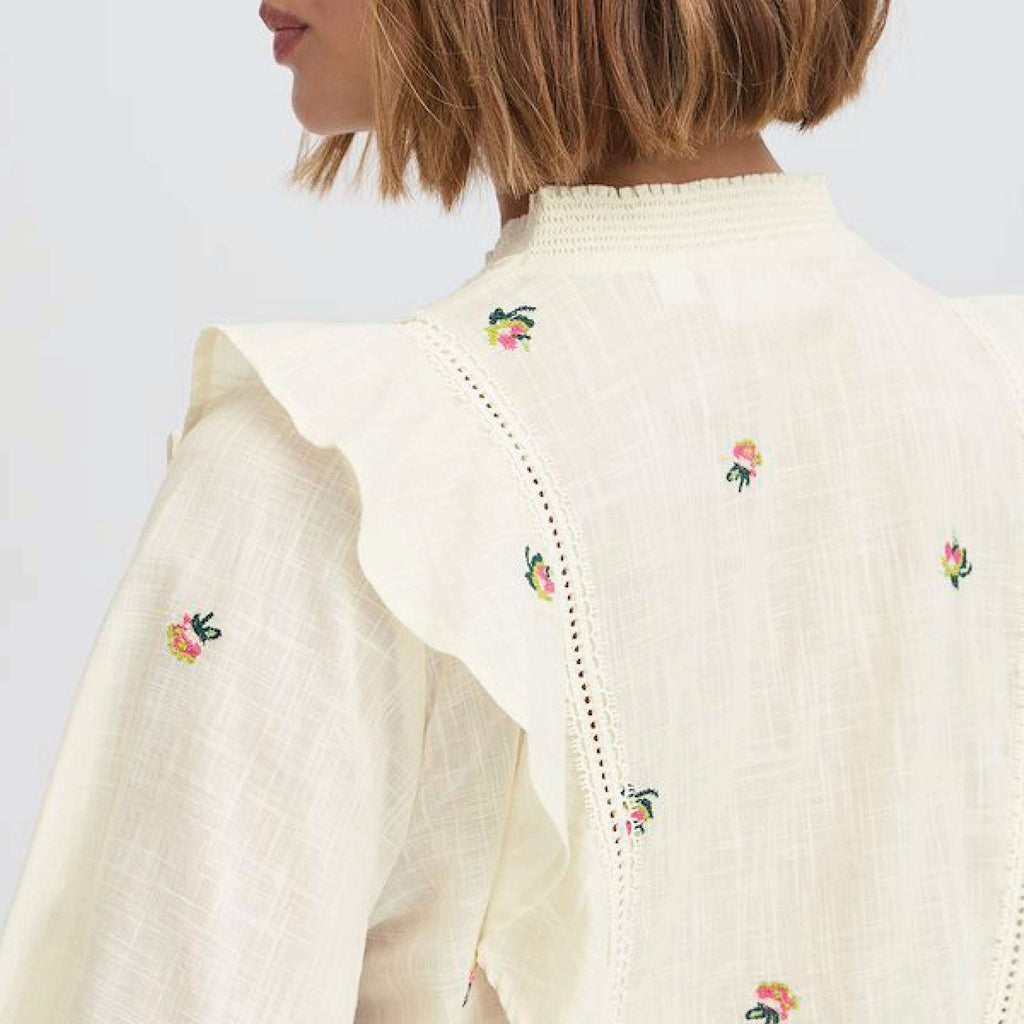 Cream-colored floral-embroidered Atelier Reve Birch Olivia Blouse with ruffle details and long sleeves.