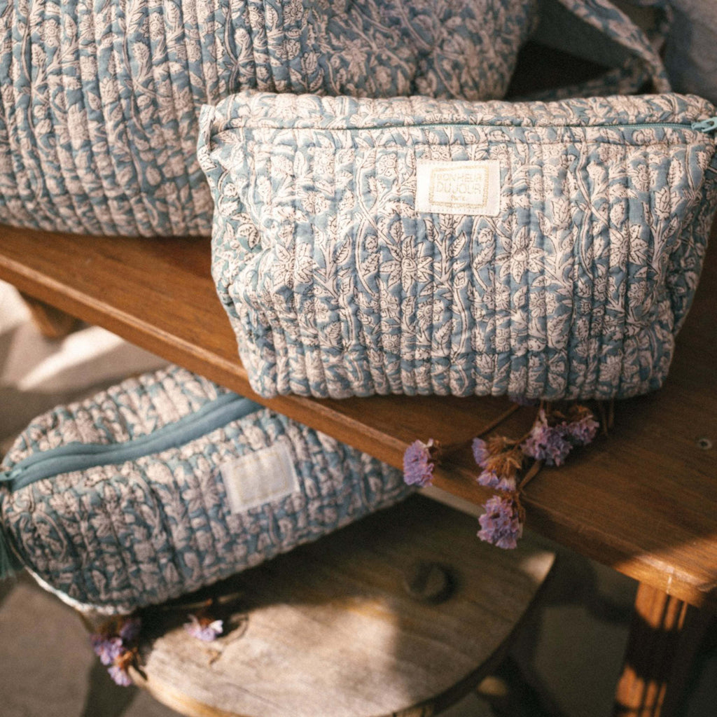 Goa Blue Green Indi Wash Bag with floral print and handmade pompons on a wooden table.