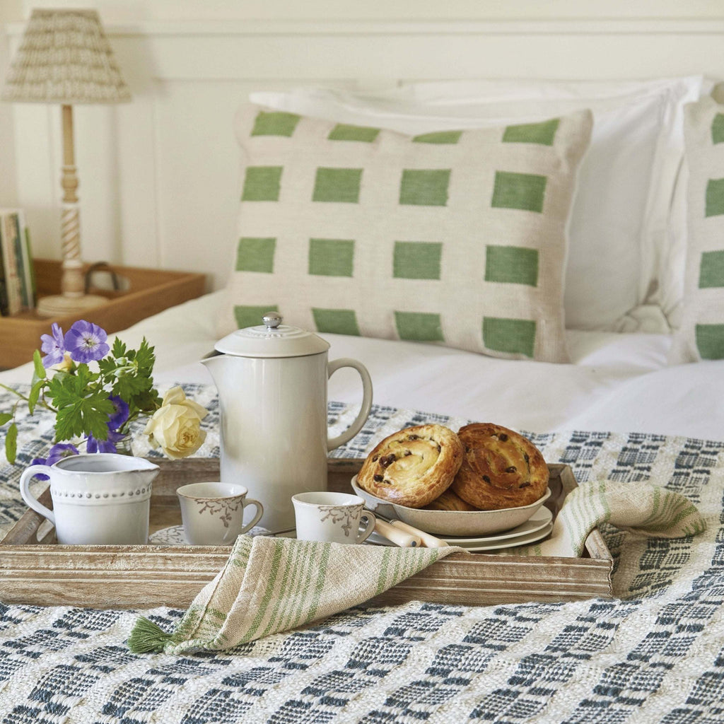 Green Faro Cushion with high-quality yarn and intricate weave on a bed with breakfast tray.