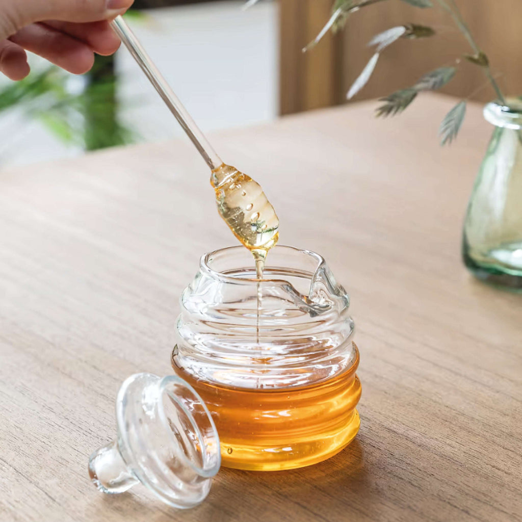 Murcot Glass Honey Pot with dibber on wooden table, showcasing transparent hand-blown recycled glass design.