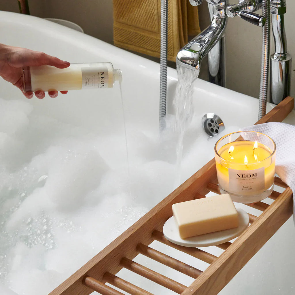 NEOM Real Luxury Bath Foam 200ml with calming candle beside relaxing bath.