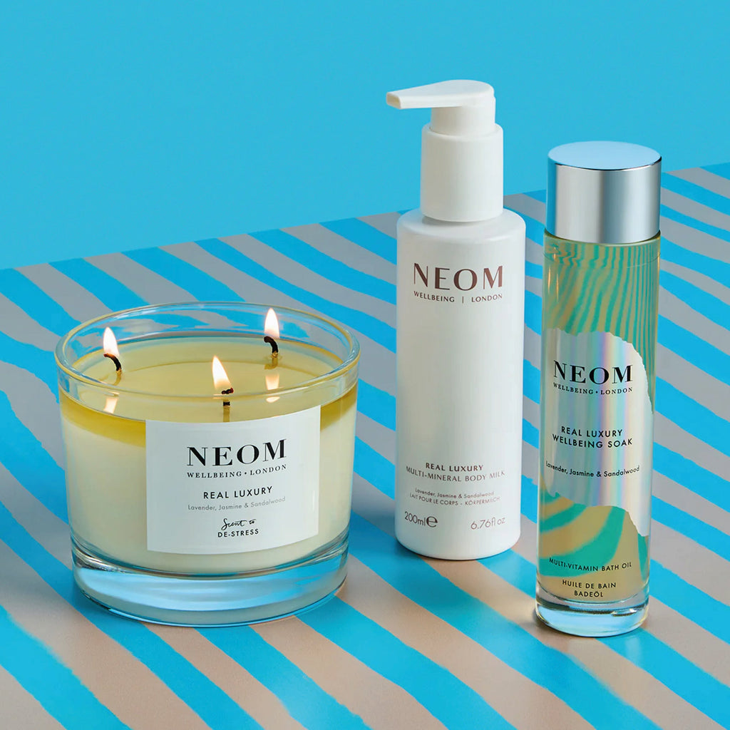 NEOM Real Luxury Wellbeing Soak 100ml with candle and lotion on striped surface.