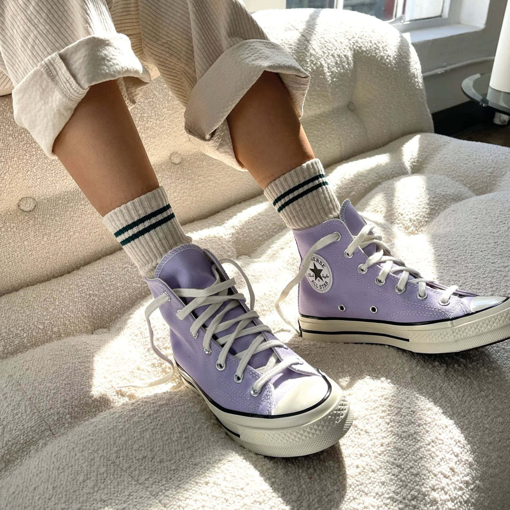 Person wearing Le Bon Shoppe Oatmeal Boyfriend Socks with purple sneakers and rolled-up pants, sitting on a couch.