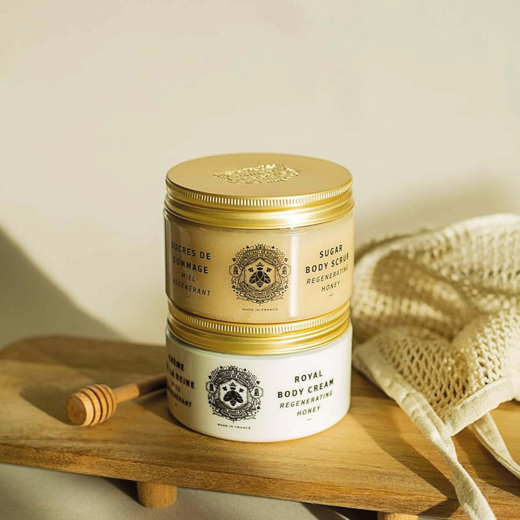 Panier Des Sens Honey Body Sugar Scrub 300g on wooden board with honey dipper and exfoliating cloth.