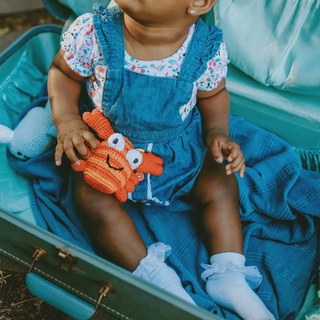 Baby holding a handmade Red Crab Baby Rattle in a suitcase.