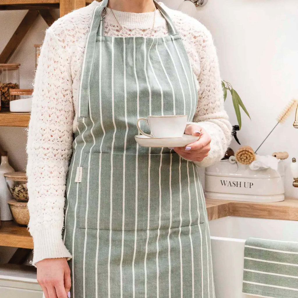 Rosemary Bampton Apron in green and white stripes with a front pocket, worn by a person in a kitchen setting.