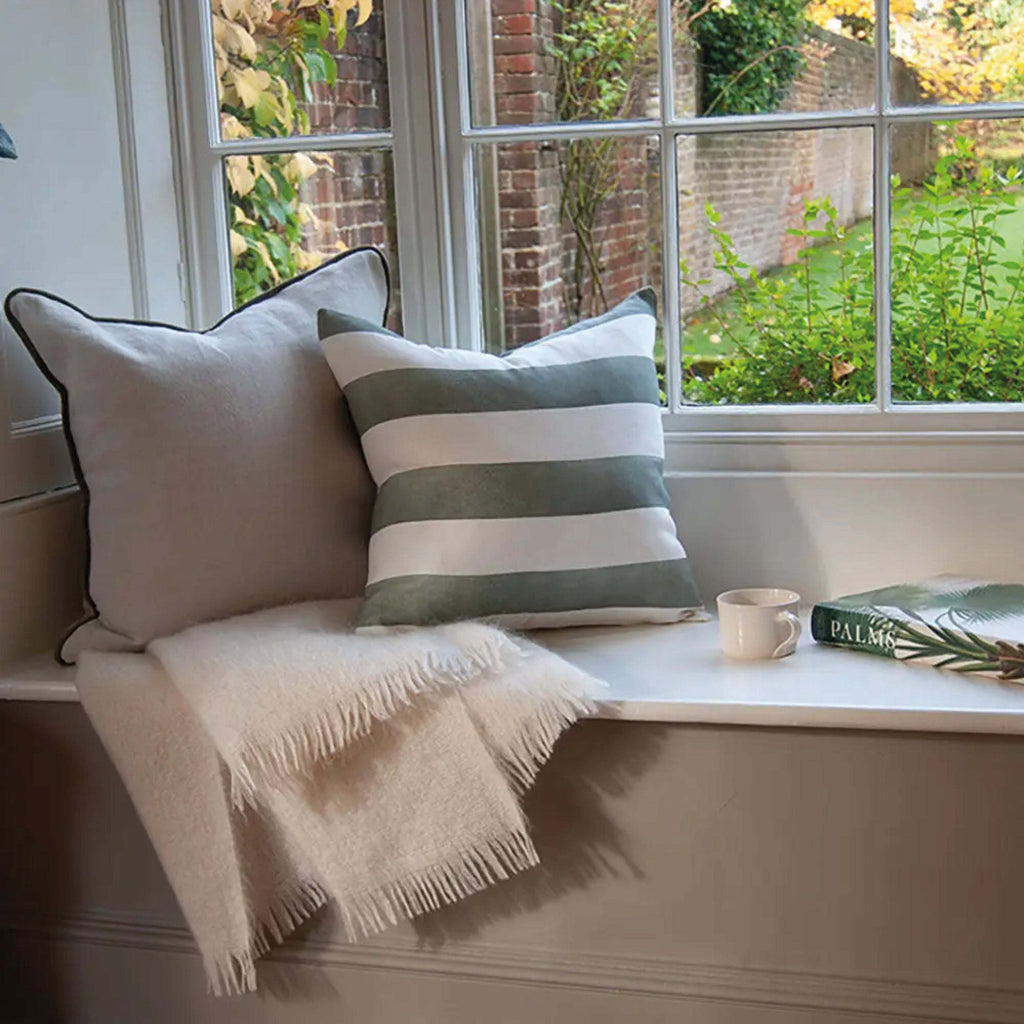 Sage Riviera Striped Linen Cushion on window seat, featuring wide green and white stripes, adds elegance and comfort to home decor.