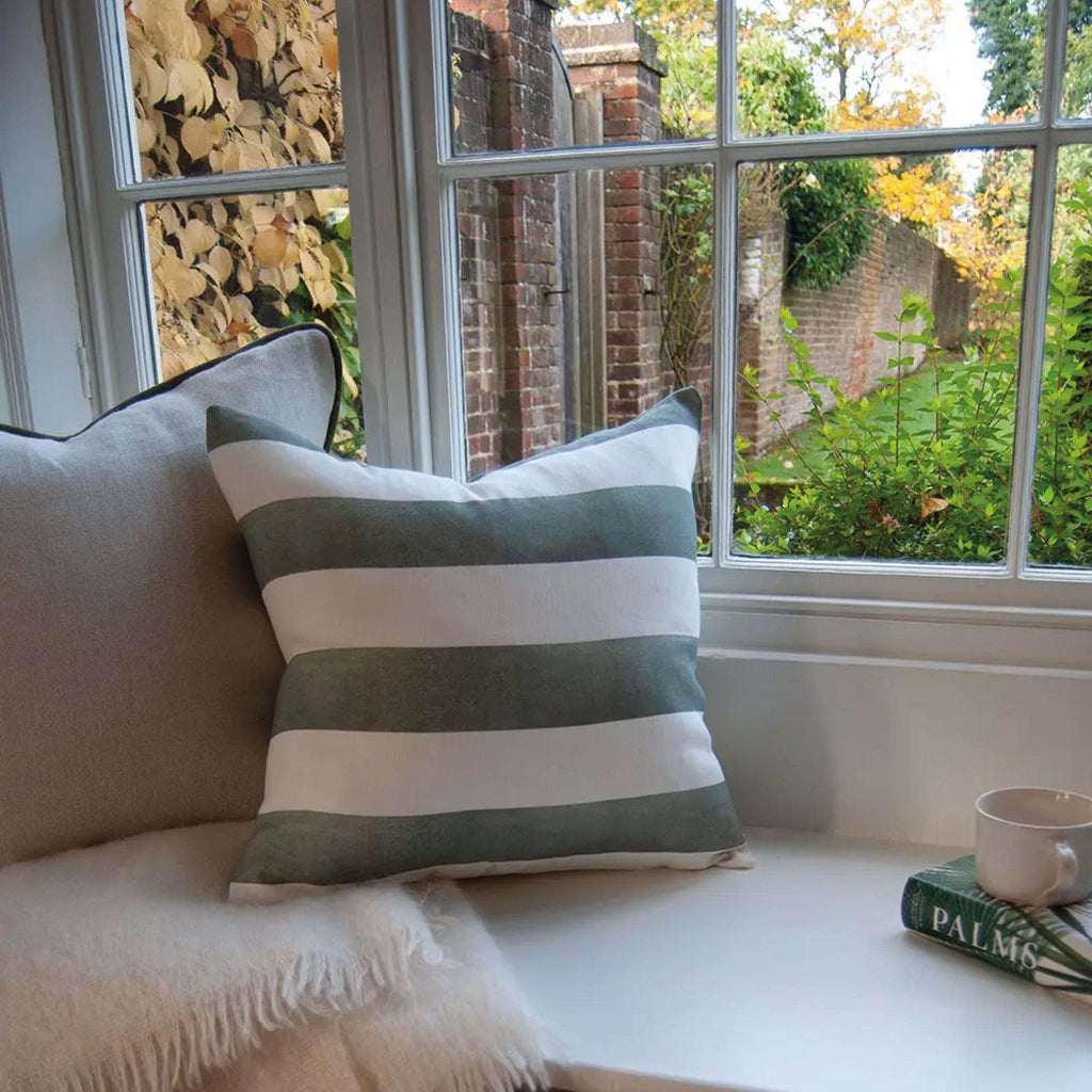 Sage Riviera Striped Linen Cushion on window seat with outdoor view, featuring wide sage and white stripes.