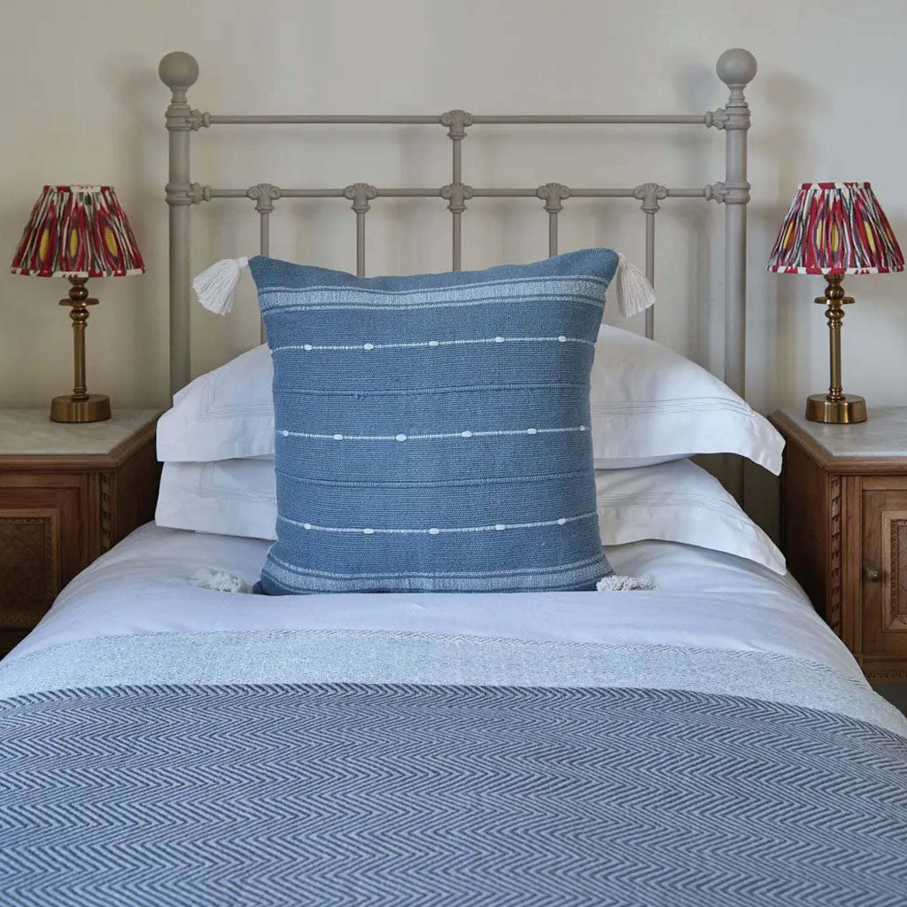 Sky Blue Tassel Cushion with slub yarn weave and striped design on a bed.