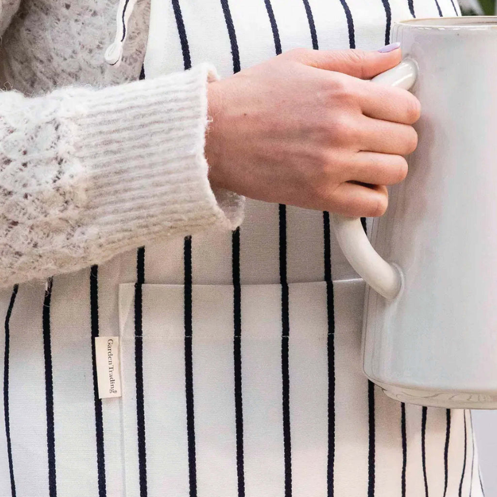 Warm White Bampton Apron with black stripes and front pocket, worn by person holding a white jug.